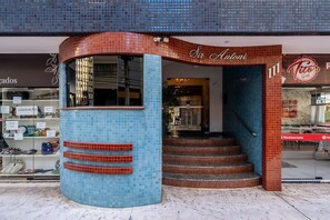 Fachada de un edificio con azulejos azules y rojos, una escalera que conduce al interior y un letrero de restaurante visible al fondo.