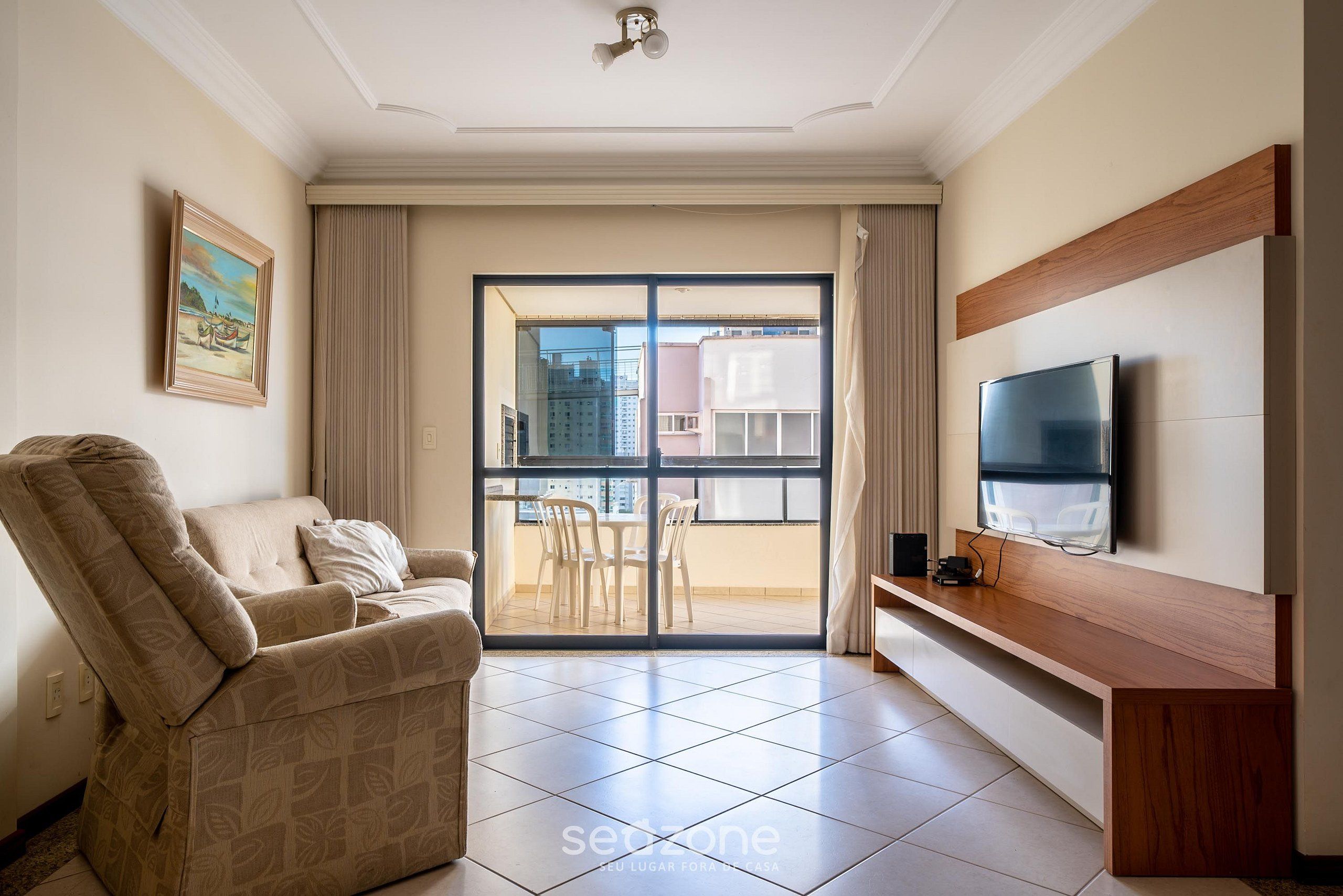 Ein modernes Wohnzimmer mit einer Couch, einem an der Wand montierten Fernseher und einem Balkon mit Blick auf die Stadt.