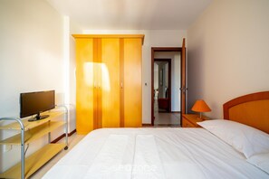 A hotel room with a bed, a TV on a stand, a wardrobe, and a bedside table with a lamp. - Sea View Apartm. 130m From the Beach in BC Esa901 (Balneário Camboriú)