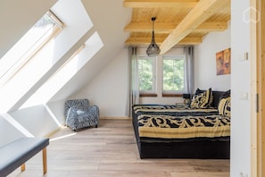 Ein Schlafzimmer mit schrägverdeckter Decke, einem Bett mit gemusterten Betttextilien, einer Bank und einem Stuhl mit ZEBRA-Muster.