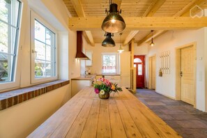 Ein Holztisch mit einer floralen Dekoration, eine Küchenzeile mit einem Fenster und ein Flur mit Holztüren.