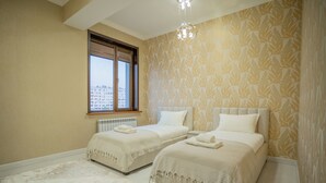 Un dormitorio con dos camas, un radiador, una ventana y un papel tapiz estampado.