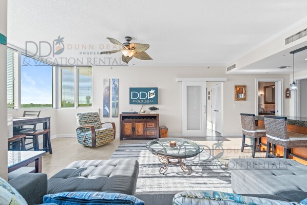 A spacious living room with a glass coffee table, comfortable seating, and a ceiling fan. - Ocean Club 403 | Enjoy Views of the Gulf! (Biloxi)