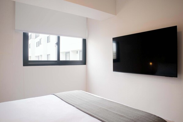 A modern hotel room with a large bed, a flat-screen TV mounted on the wall, and a window providing a view of the building outside. - w Bright 2BR w Balconny in Miraflores (Lima)