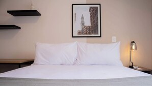 A neatly made bed with white linens, a framed cityscape picture on the wall, and a bedside lamp. - w Bright 2BR w Balconny in Miraflores (Lima)
