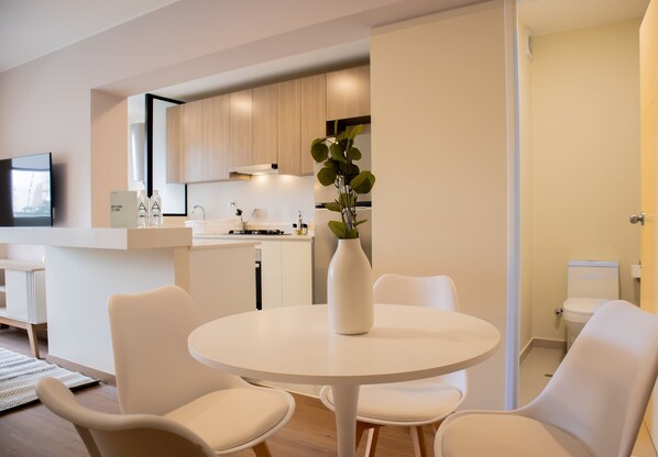 A modern kitchen with wooden cabinets, a white countertop, and a dining area with a round table and white chairs. - w Enchanting 2BR w Balcony Near Kennedy Park (Lima)