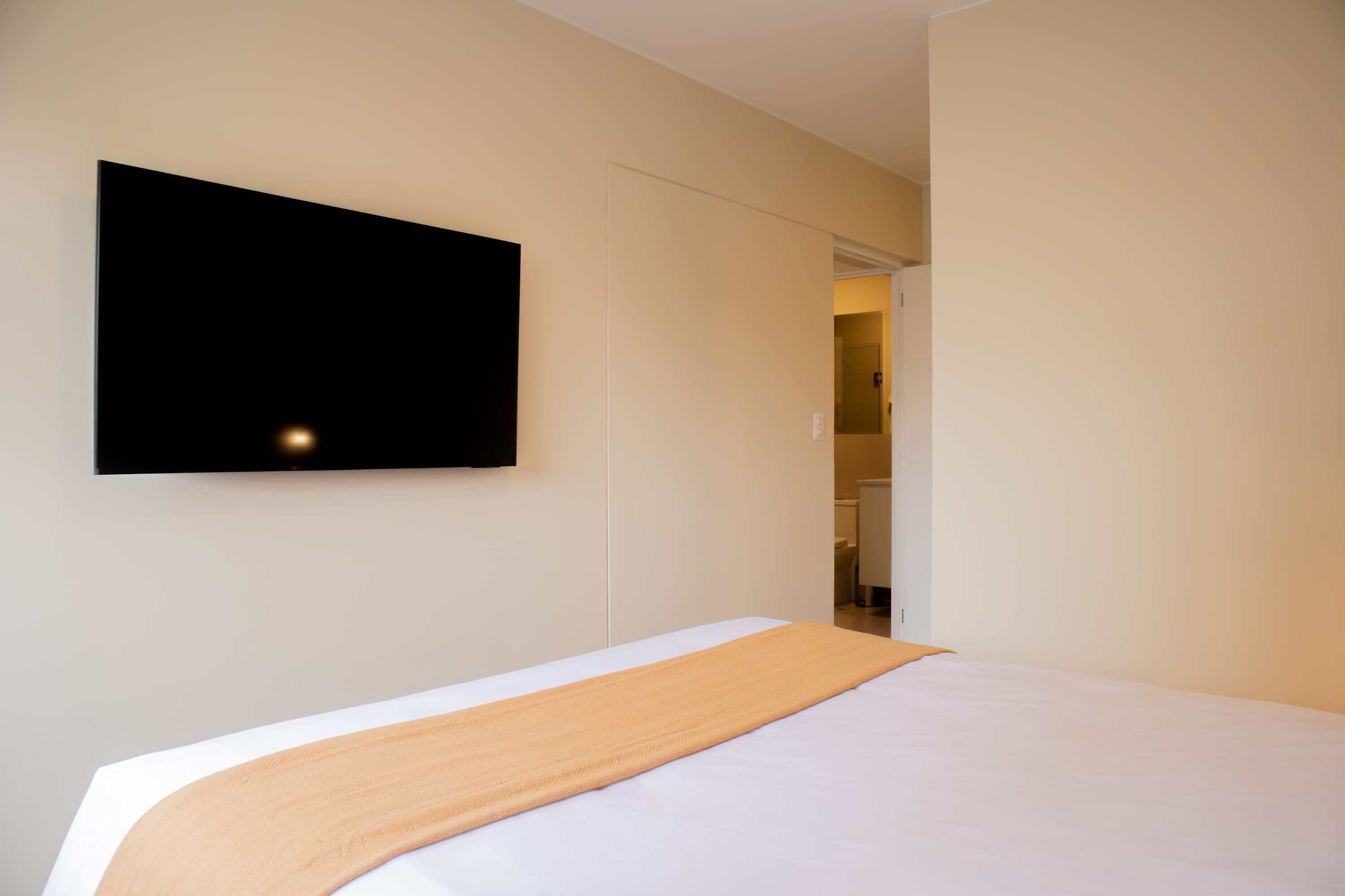A hotel room with a bed, a television mounted on the wall, and a door leading to a bathroom.