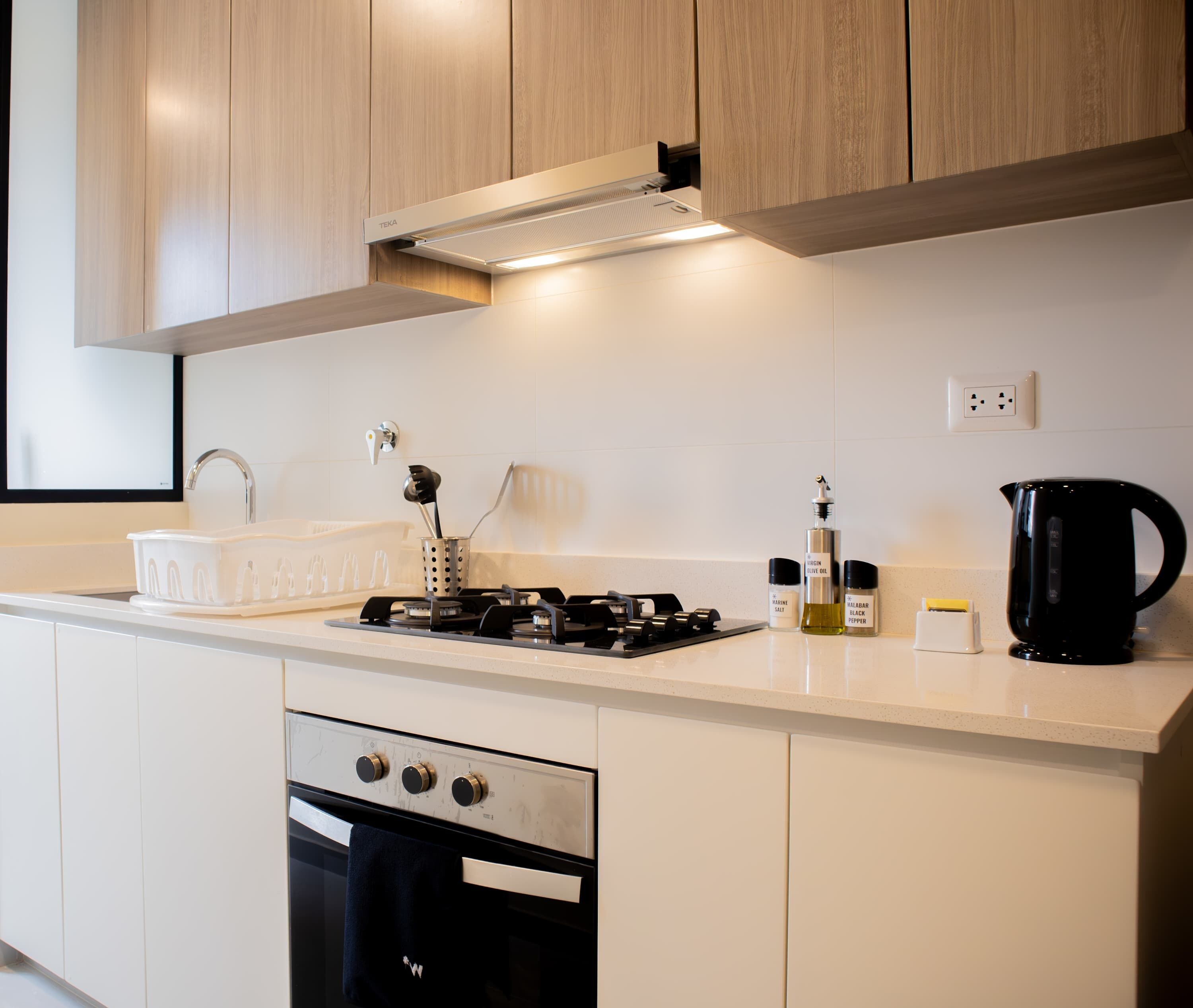 Una cocina moderna con armarios blancos, estufa a gas, horno integrado y cafetera.