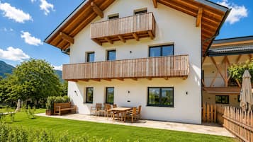 Een gebouw met twee verdiepingen, een balkon, een terras met buitenmeubilair en een verzorgd gazon.