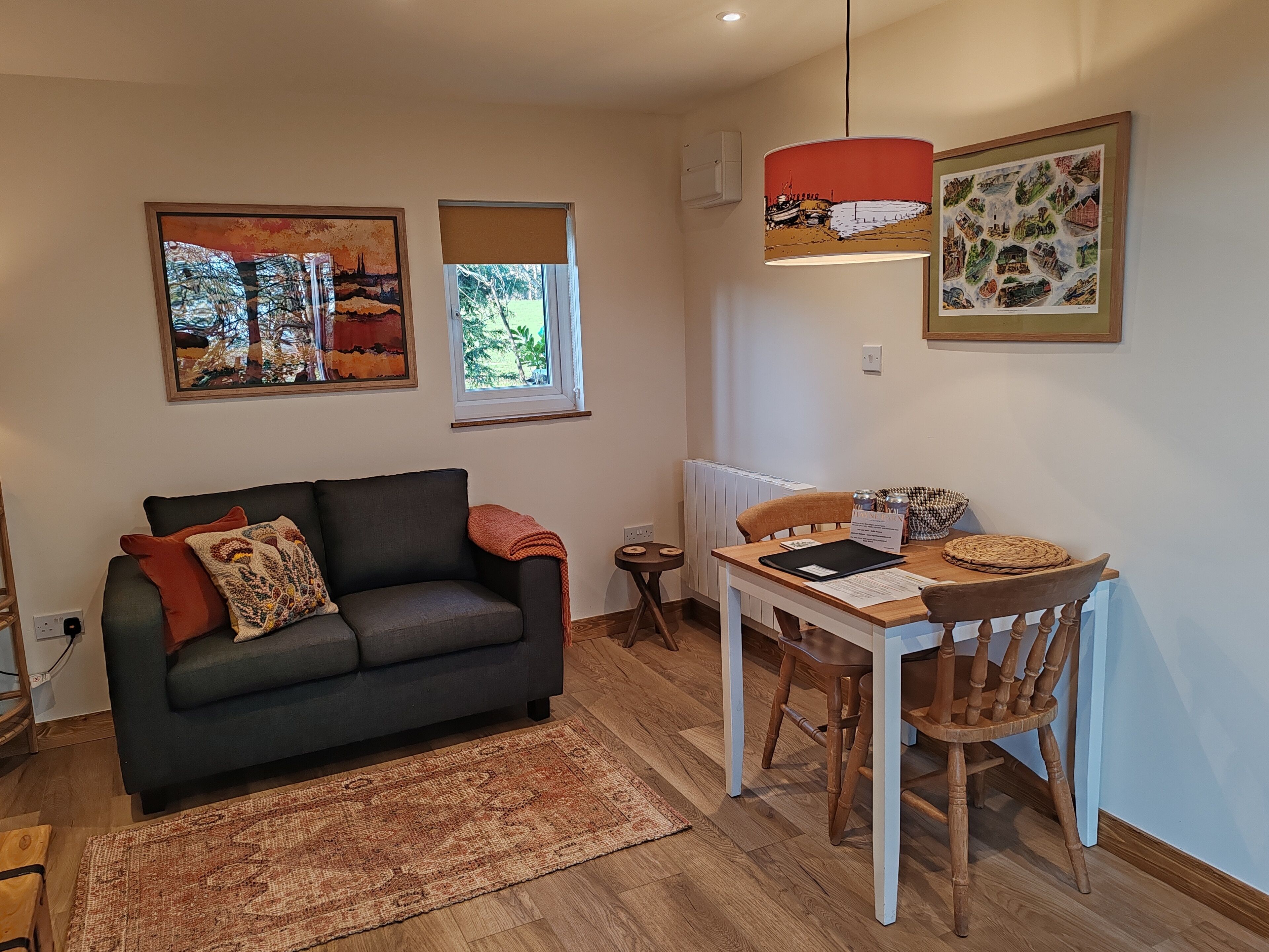 Un salón acogedor con un sofá gris oscuro, un tapete estampado y una mesa de comedor con sillas de madera.