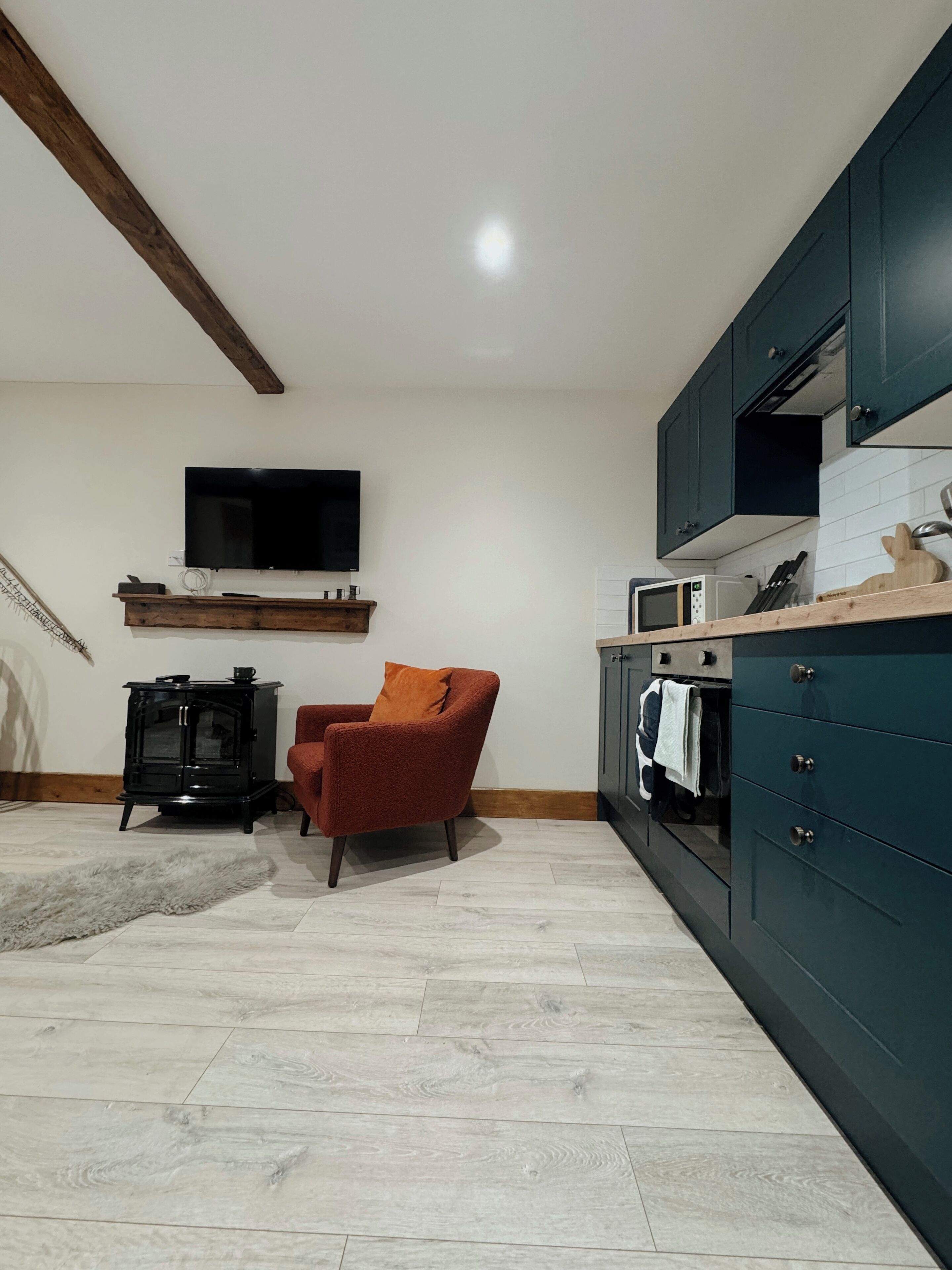 A modern kitchen with dark cabinets, a microwave, and a stove. There is a red chair and a small black stove in the corner.