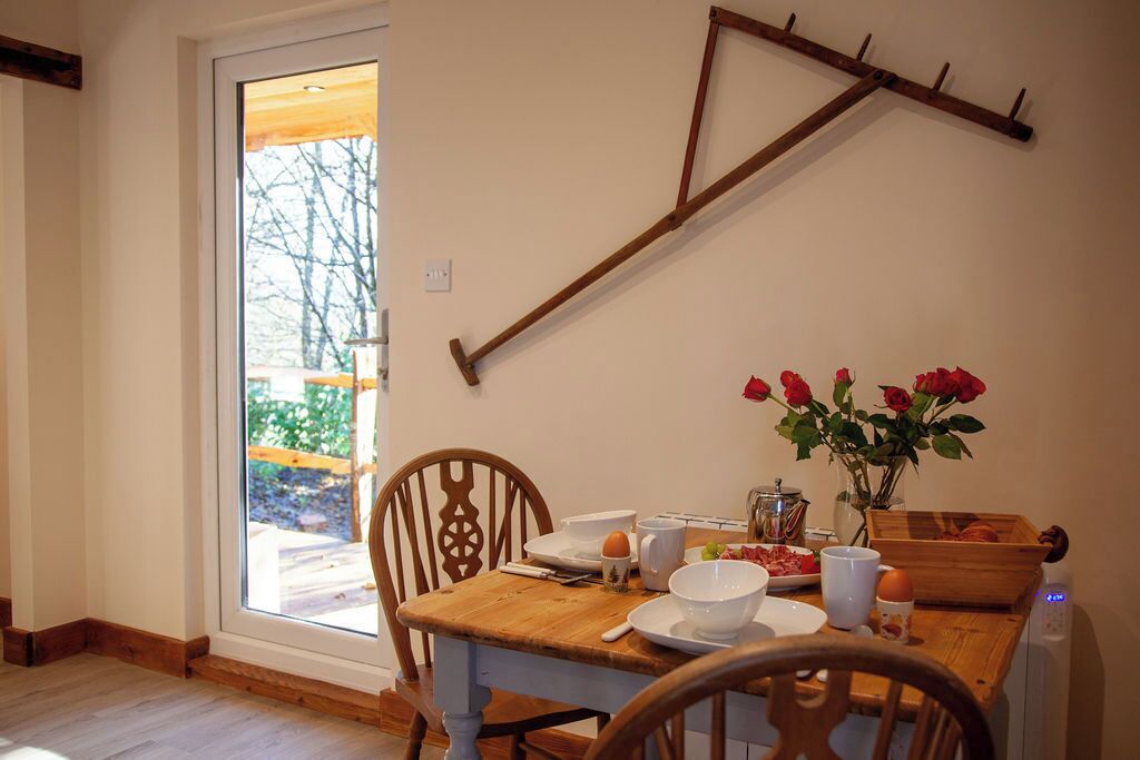 A dining area with a wooden table, chairs, a window with a view of trees, and a wall-mounted wooden rack.