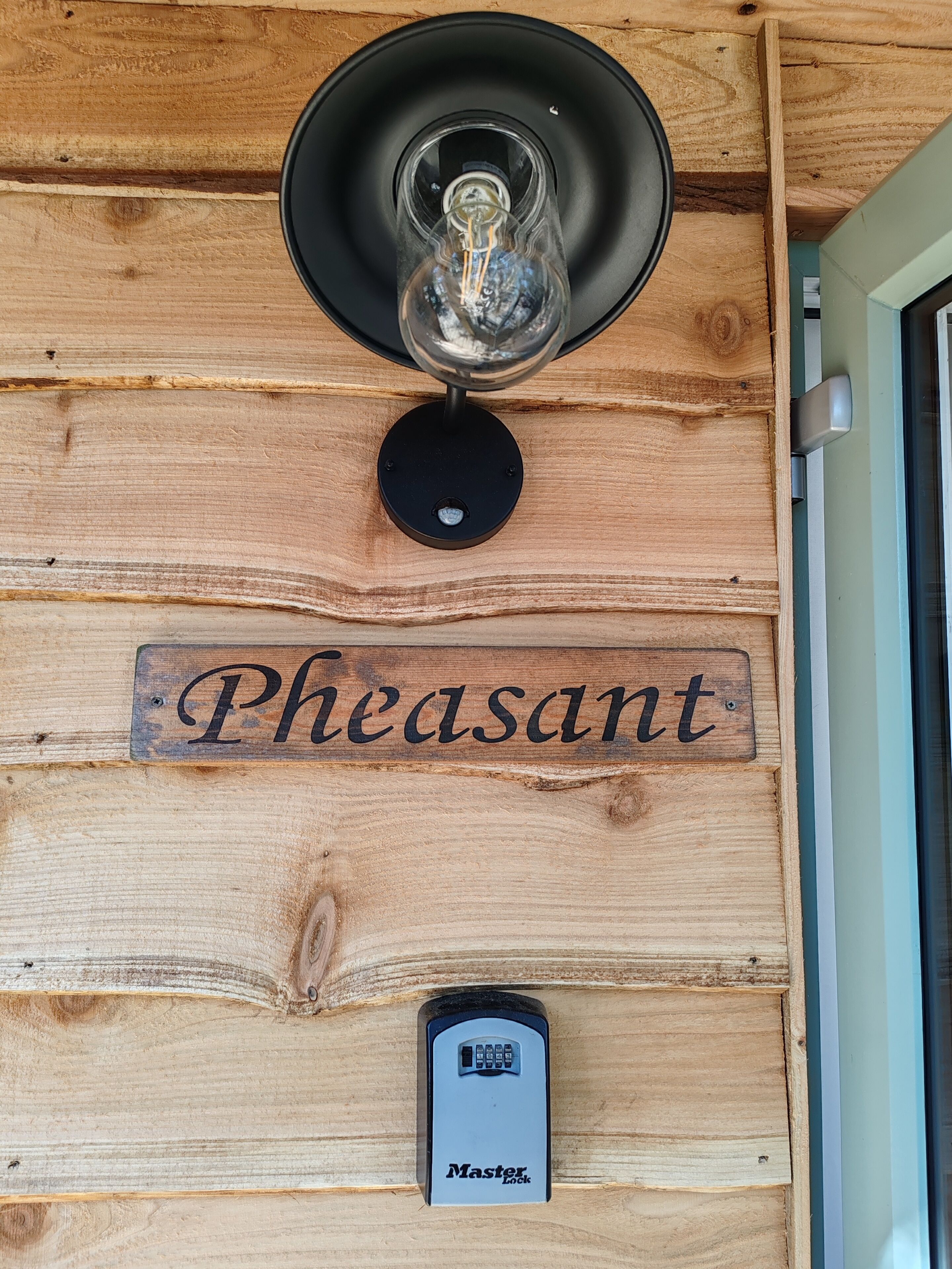 Puinen seinä, jossa on valaisin, kyltti, jossa lukee ”Pheasant”, ja Master Lock -turvalukko.