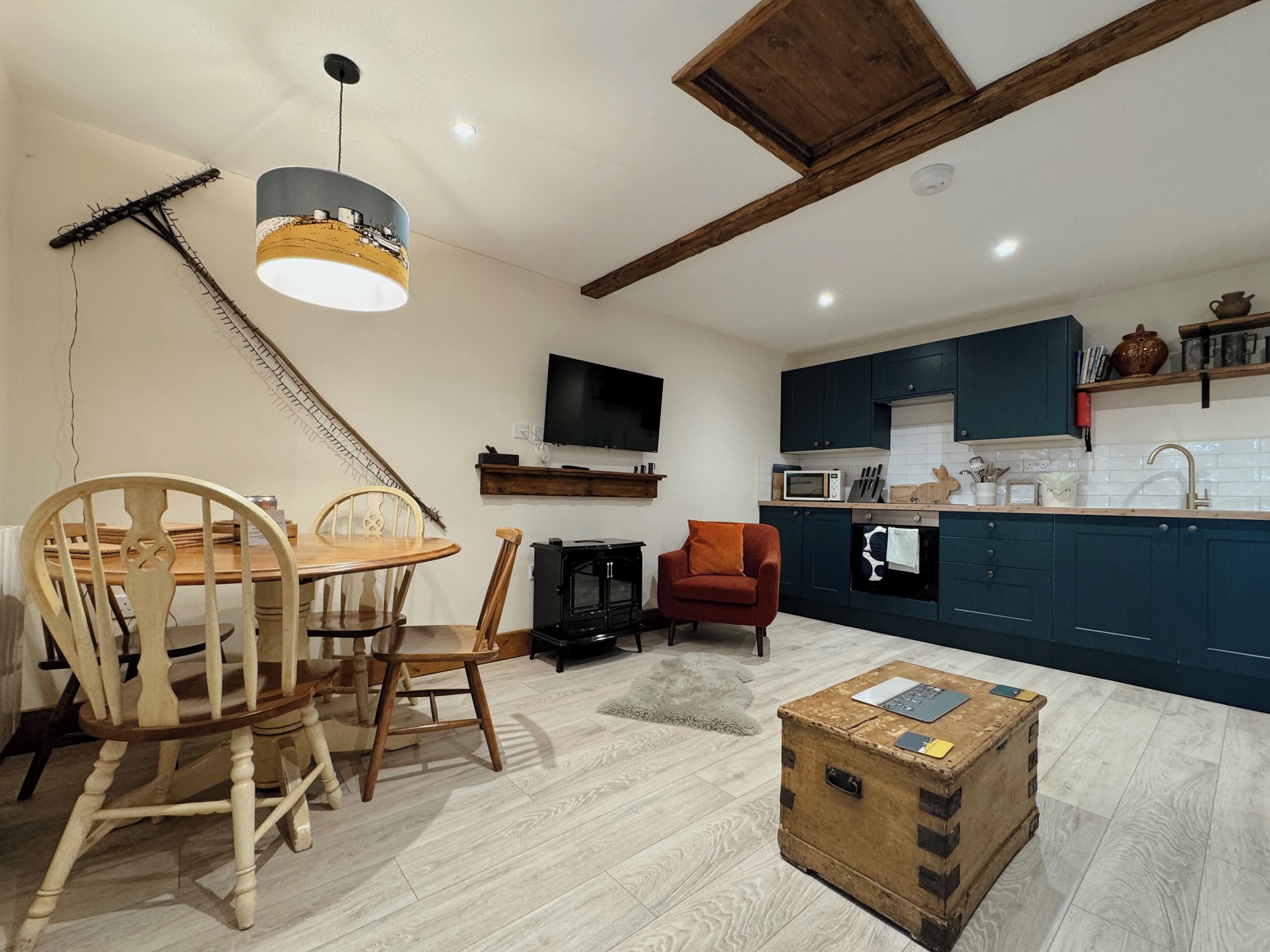 Un espace de vie compact comprenant un coin repas, un canapé, un téléviseur et une cuisine dotée de meubles sombres et de plans de travail blancs.