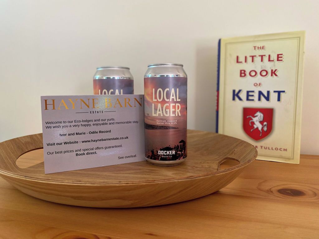 Ein Holztablett mit einem Buch mit dem Titel „The Little Book of Kent“, einer Dose „Local Lager“ und einem Schild für Hayne Barn Estate.