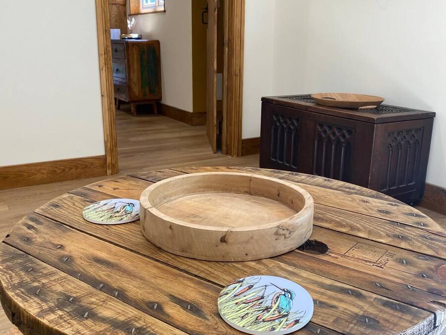 A round wooden table with a central bowl and two decorative plates, a television mounted on the wall, and a wooden cabinet in the background.