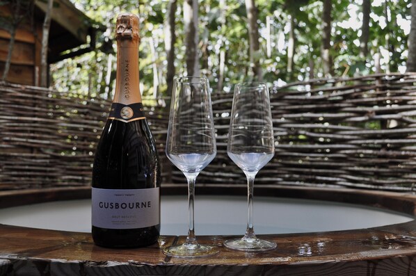 Una botella de vino espumoso GUSBOURNE Brut Reserve y dos copas de vino vacías sobre una mesa redonda de madera con un fondo tejido.