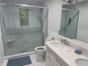 Casa de banho moderna com cabine de duche em vidro, sanita, lavatório e um espelho grande.
