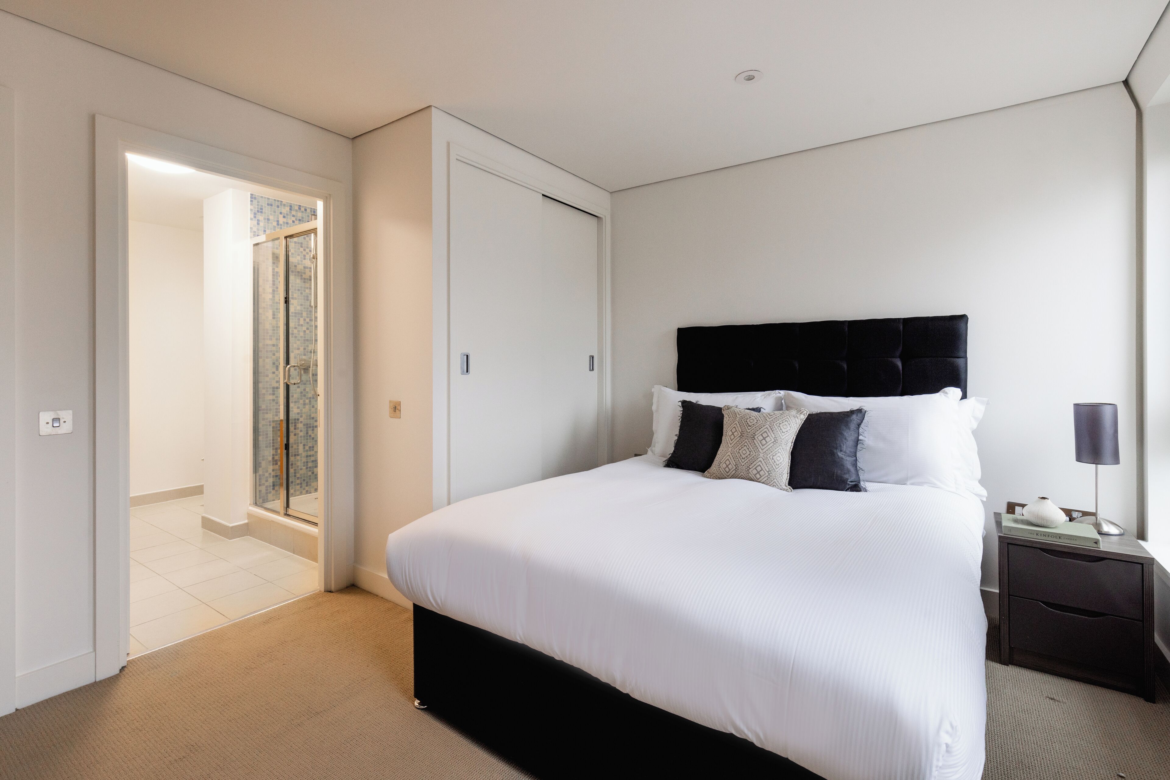 A modern bedroom with a large bed, a dark headboard, and a bedside table with a lamp.