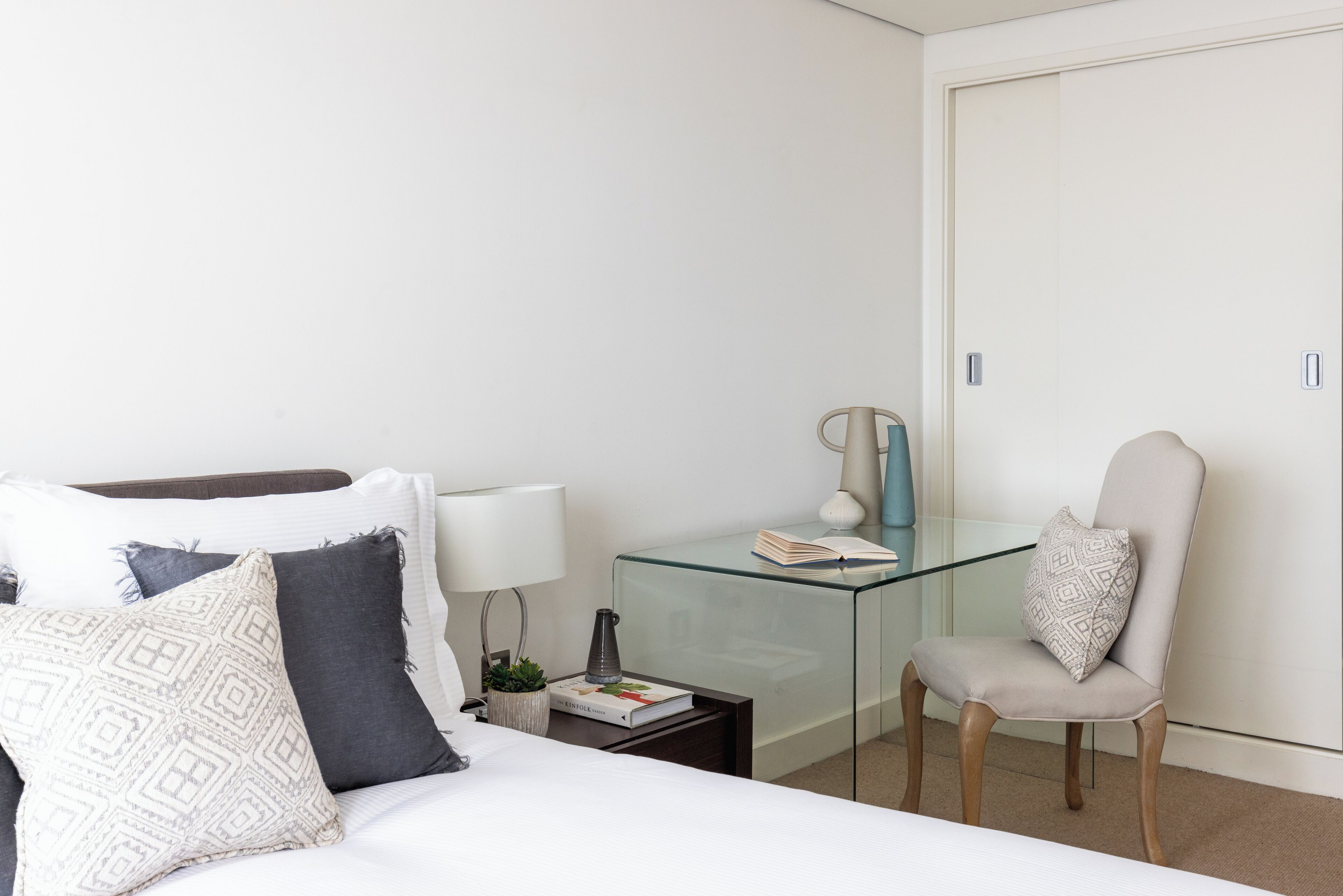 A modern hotel room with a bed, a glass desk, a chair, and a wardrobe.