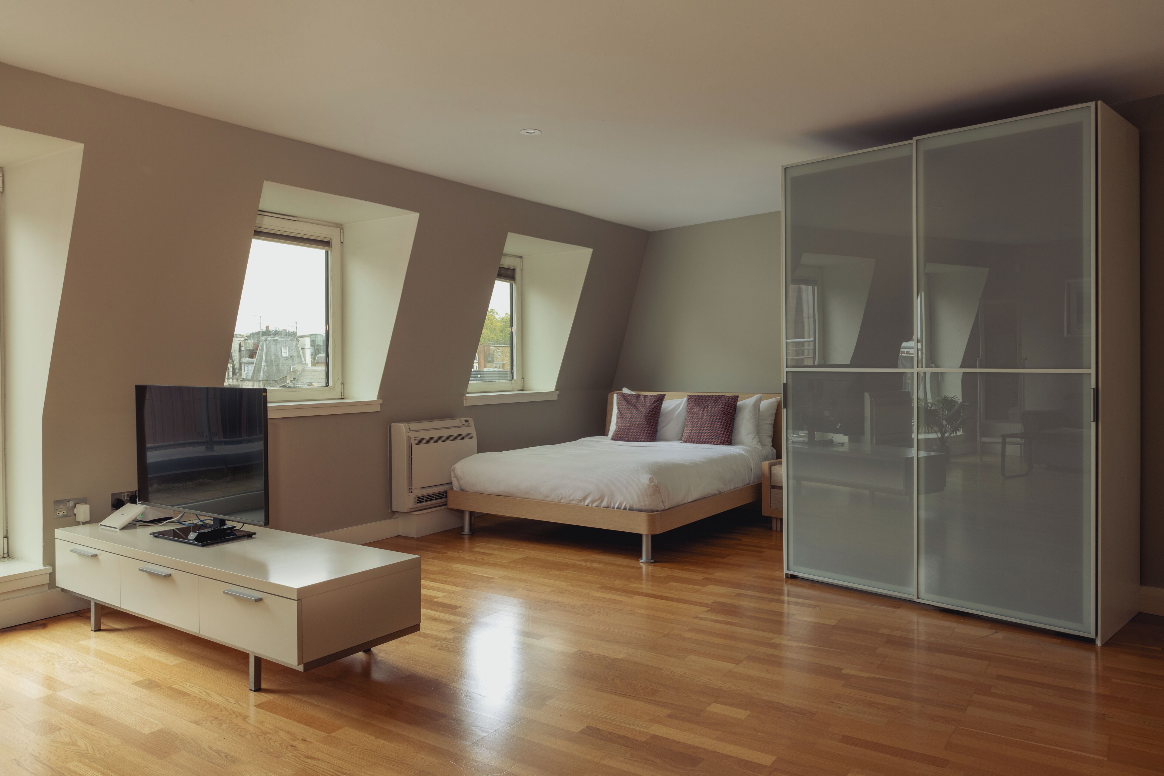 A modern bedroom with a bed, a wardrobe, a desk, and a TV.