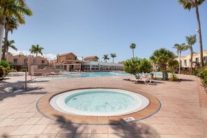 A resort with a swimming pool, lounge chairs, and palm trees.