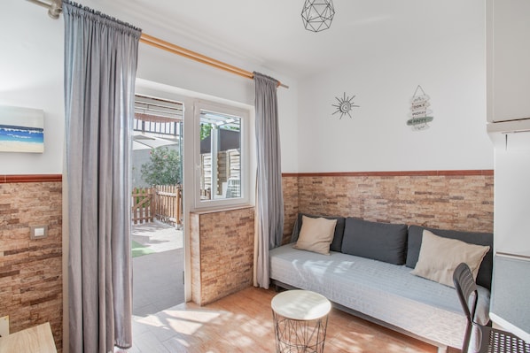 A room with a brick wall, a sofa, a small table, and a window with curtains.