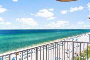 Ein Strand mit klarem türkisblauem Wasser, weißem Sand und einem Balkon mit Blick auf die Szene.