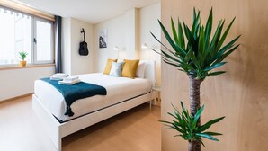 Quarto moderno com cama, almofadas, um violão, uma planta e uma janela.