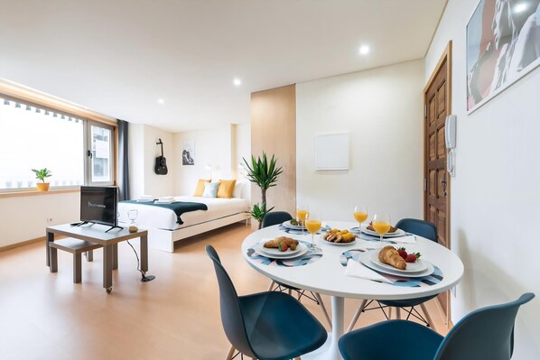 A modern living room with a sofa, a dining table with breakfast, a TV, and a guitar on the wall. - Guestready - Musichall (Porto)