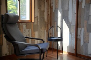 Una habitación con un muro revestido de madera, una ventana, un sillón tapizado en gris y una pequeña mesa negra.