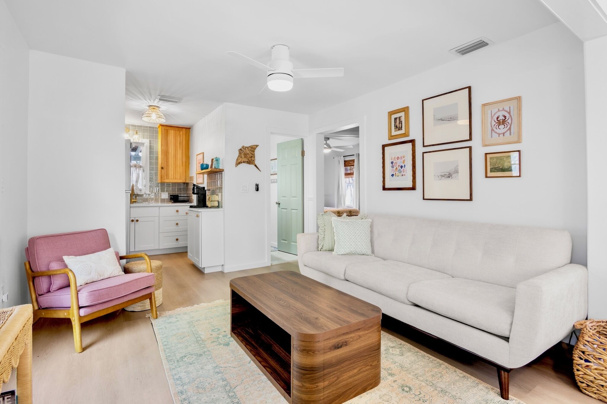 A modern living room with a white sofa, a pink armchair, a wooden coffee table, and a kitchen in the background.