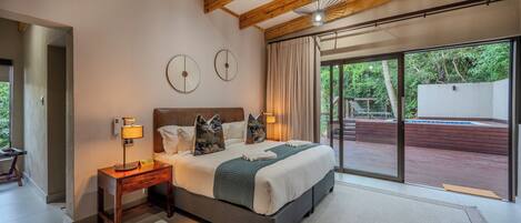 A bedroom with a large bed, wooden headboard, bedside lamps, and a view of a deck through glass doors.
