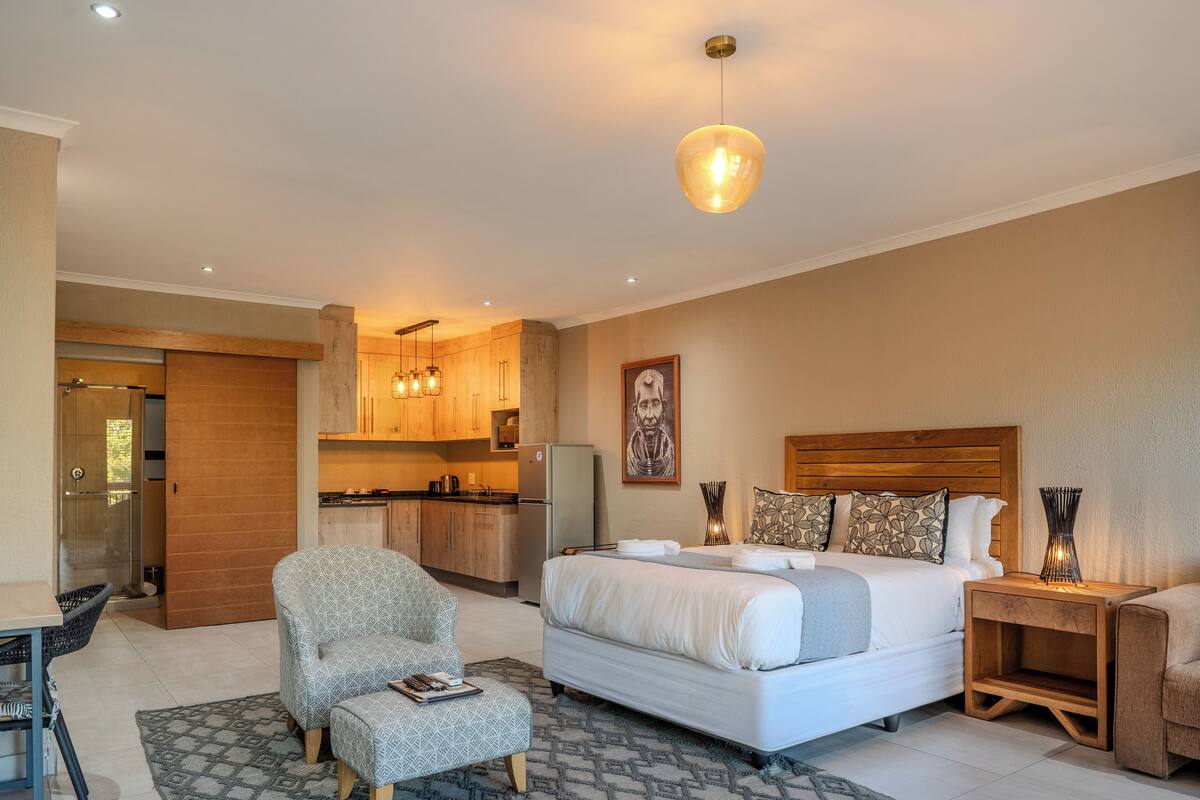 Ein Schlafzimmer mit einem großen Bett, Nachttischen und einem Beistelltisch. Ein Sessel und ein kleiner Tisch mit einer Zeitschrift stehen im Raum. Das Zimmer verfügt über einen Holzkopfseitenverkleidung und ein Bild an der Wand.