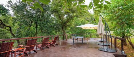 Une terrasse en bois, agréée de mobilier d’extérieur, et entourée d’une végétation luxuriante.