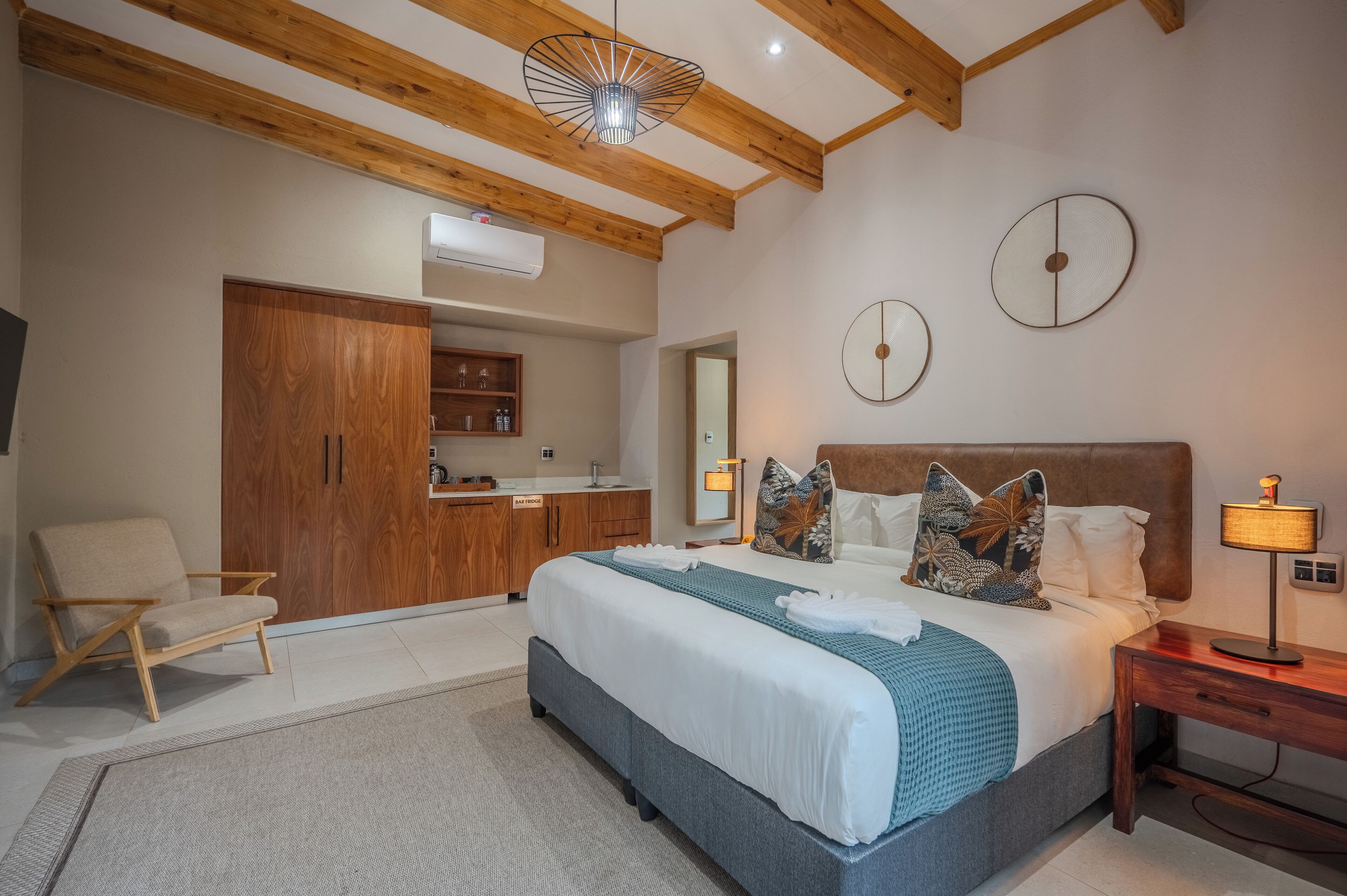 Quarto com cama, mesa de cabeceira, abajur e guarda-roupa de madeira.