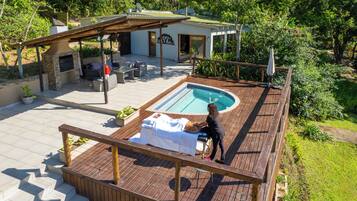 Un espace piscine doté d’une terrasse en bois, d’une chaise longue et d’une personne debout près de la piscine.