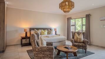 A hotel room with a bed, two armchairs, a coffee table, a lamp, and a large window with curtains.