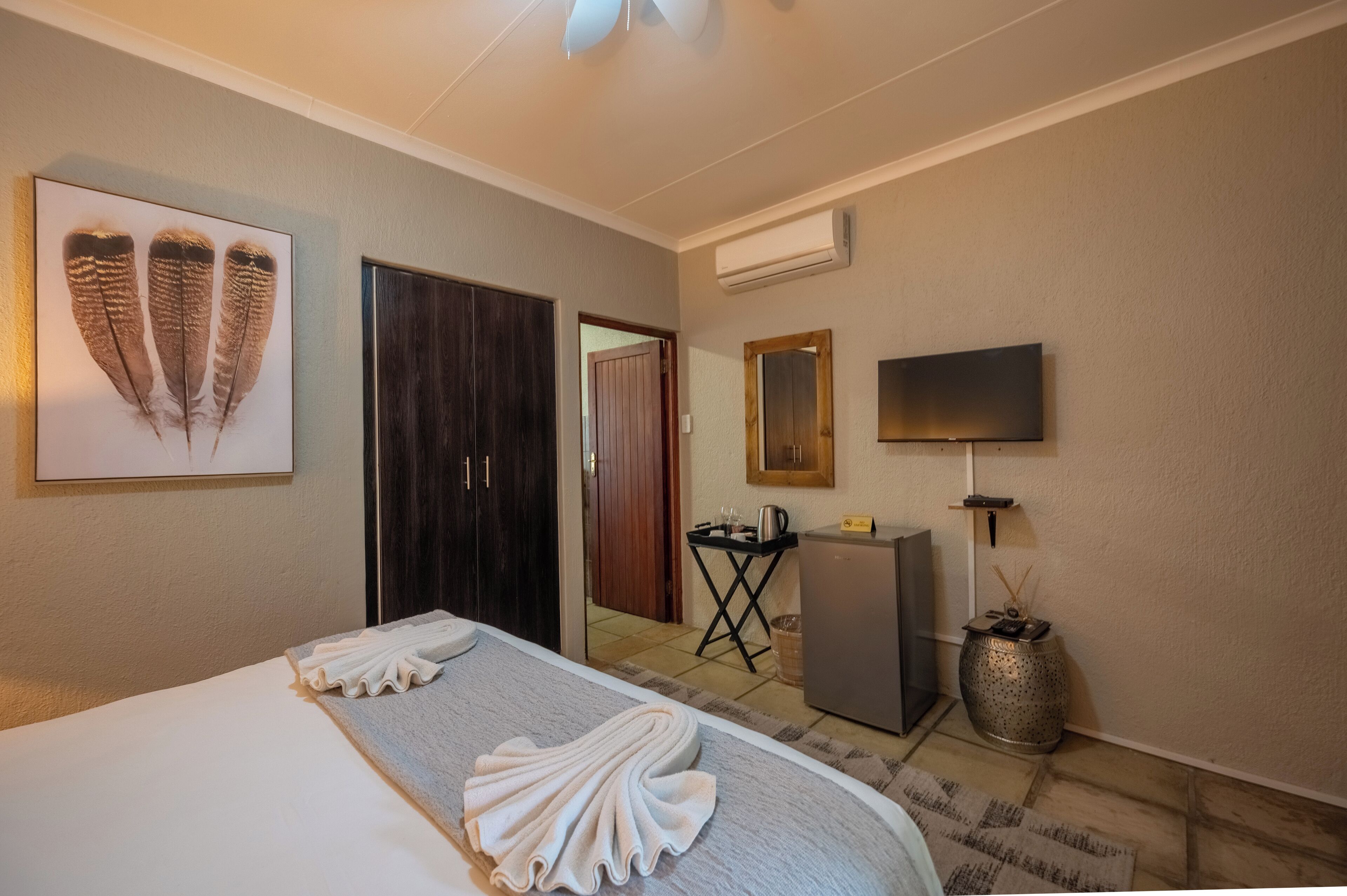 Une chambre d’hôtel comprenant un lit, une télévision, un climatiseur fixé au mur, une œuvre d’art encadrée et une porte donnant sur une autre pièce.
