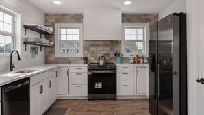 Cocina moderna con armarios blancos, refrigerador de acero inoxidable, horno empotrado y salpicadero de piedra.