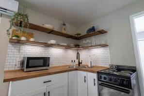 Een moderne keuken met witte kastjes, een magnetron, een fornuis en houten planken met decoratieve objecten.