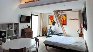 A loft-style bedroom with a high ceiling, a bed, a treadmill, and a dining area with a table and chairs. - Wooden cottage (Longuenesse)