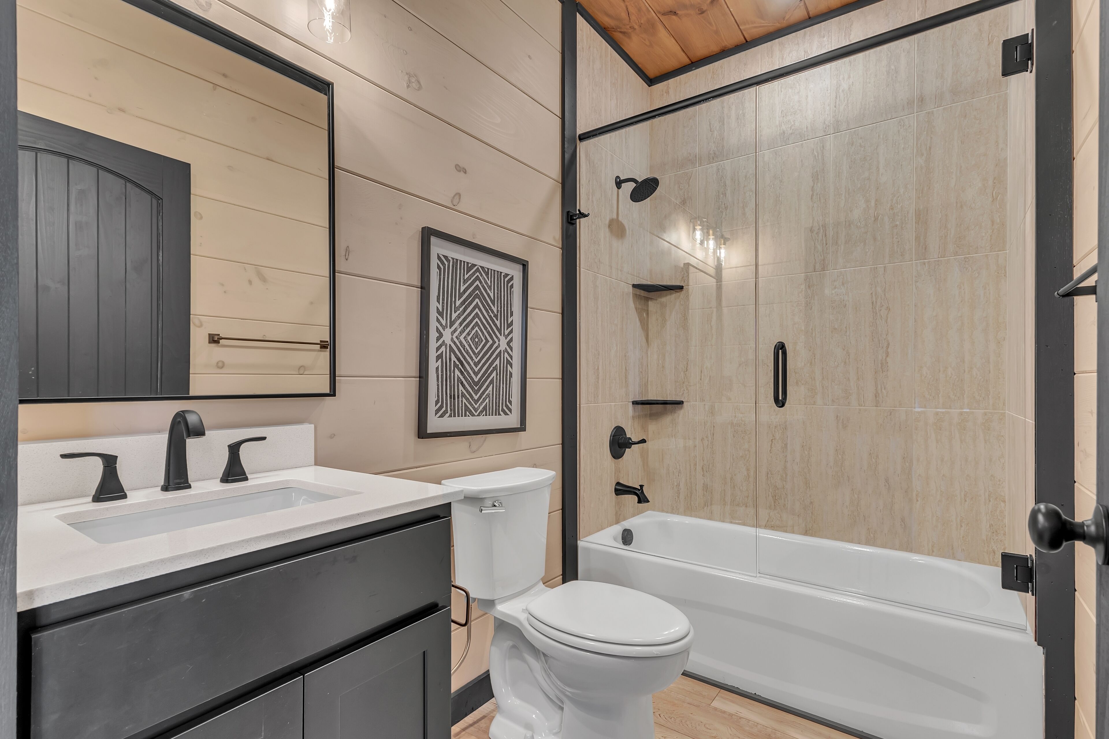 Une salle de bain moderne avec un lavabo blanc, des robinets noirs, des toilettes et une douche à parois de verre.