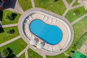 An aerial view of a swimming pool with lounge chairs and umbrellas, surrounded by a paved walkway and greenery.