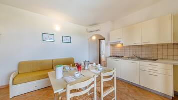 Un espacio habitable compacto con kitchenette, una mesa de comedor con sillas, un sofá y dos cuadros en la pared.