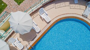 Vista aérea de una piscina con sillas de descanso blancas y sombrillas, rodeada por un solárium con baldosas.