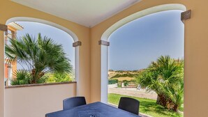 Un balcón con mesa y sillas, con vistas a un paisaje de palmeras y una colina distante.