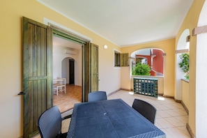 A patio with a table and chairs, an open door leading to an interior room, and a view of a balcony with plants.