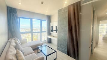 A modern living room with a sofa, a glass coffee table, and a large window offering a city view.