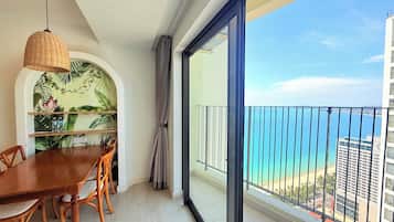 Un balcon avec vue sur la mer et les bâtiments, un coin repas avec une table et des chaises, et un luminaire suspendu.